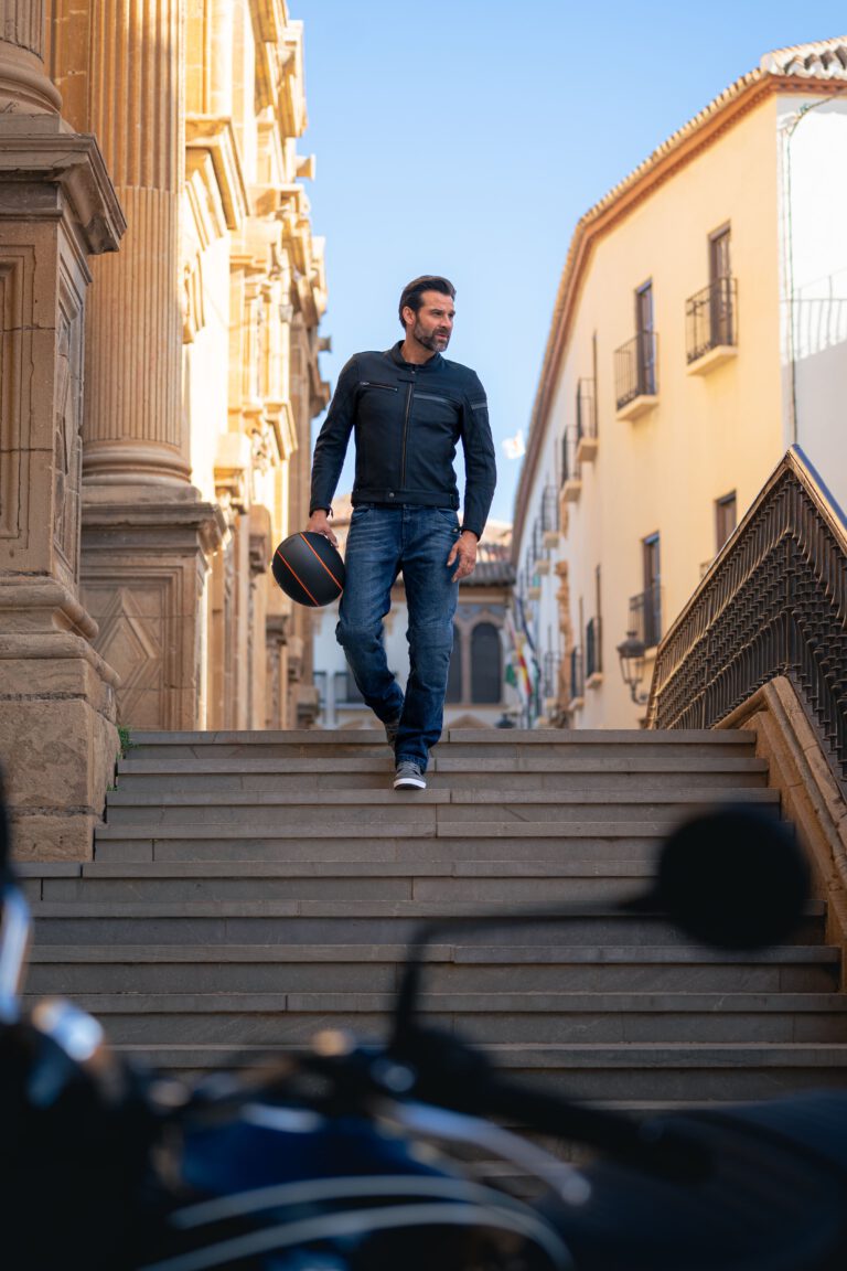 Ein Mann in Jeans, Lederjacke und einem Motorradhelm in der Hand, läuft eine Steintreppe hinunter - Lifestyle Fashion Fotograf Chris Gollhofer - Andalusien