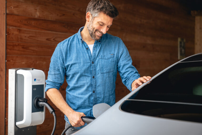 Ein Mann steckt den Ladestecker in sein Elektroauto und lacht - Chris Gollhofer Fotograf - Allgäu