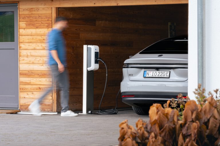 Ein Mann läuft zu seinem Elektroauto das in einem Carport geladen wird - Chris Gollhofer Lifestyle Fotograf - Europa