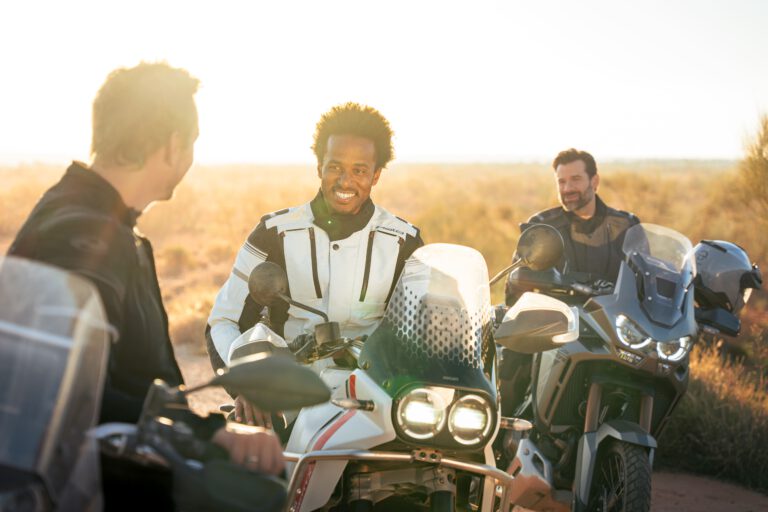 Drei Männer sitzen in der Wüste bei Sonnenaufgang auf ihren Motorrädern und lachen - Chris Gollhofer Lifestyle Fotograf Fashion - Europa